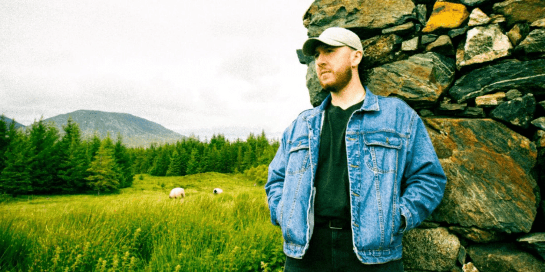 Jamie McIntyre male musician in denim jacket standing in lush green field